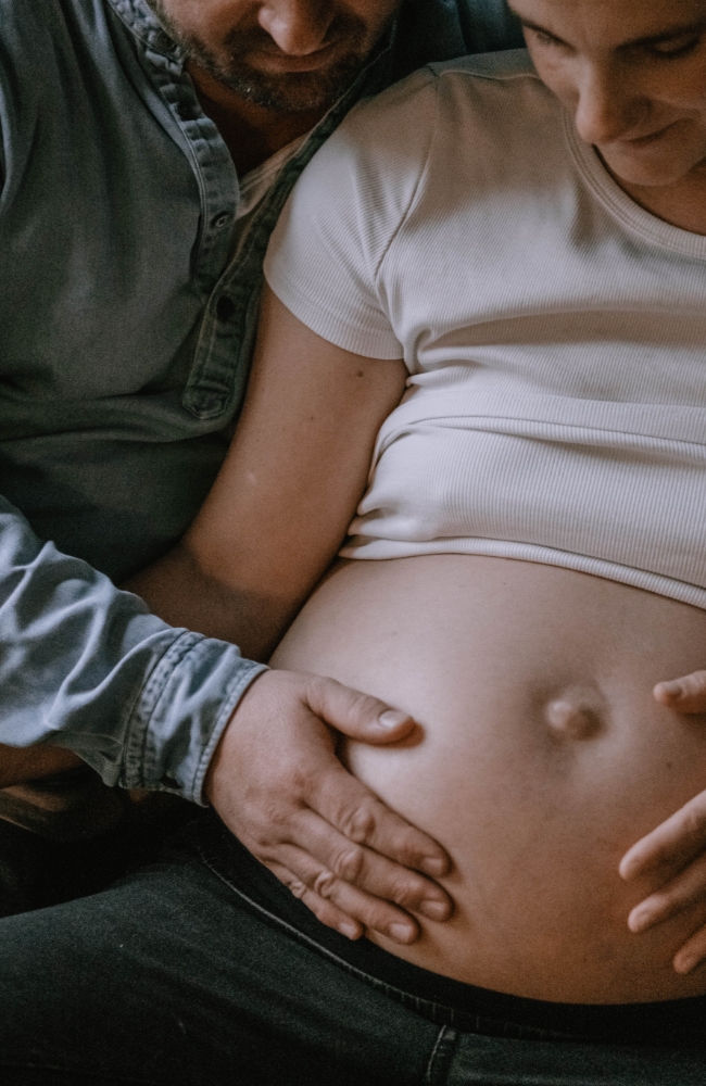 Paar in glücklicher Vorfreude auf das gemeinsame Baby. Beide halten eine Hand auf den nackten Babybauch und blicken ihn an