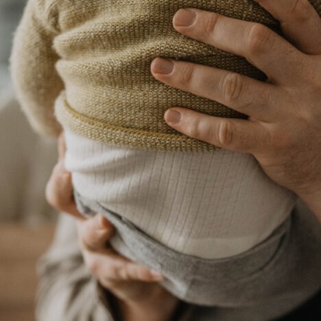 Vater hält seinen Sohn im Arm, zu sehen sind der Rücken des Babys und die Hände des Vaters